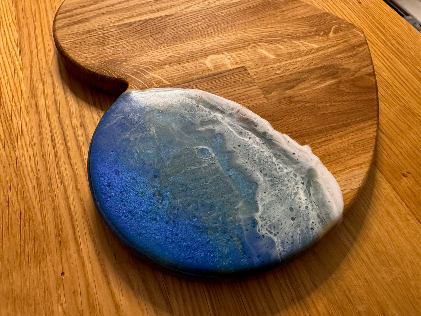 Ocean-themed resin coaster with blue and white wave design on wooden serving board