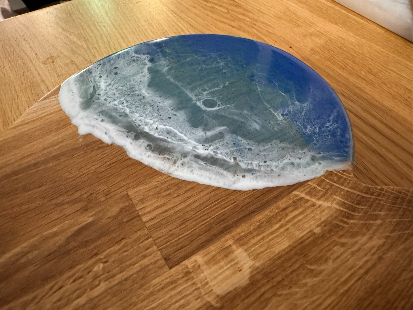 Ocean-themed resin coaster with blue waves and white foam on wooden surface